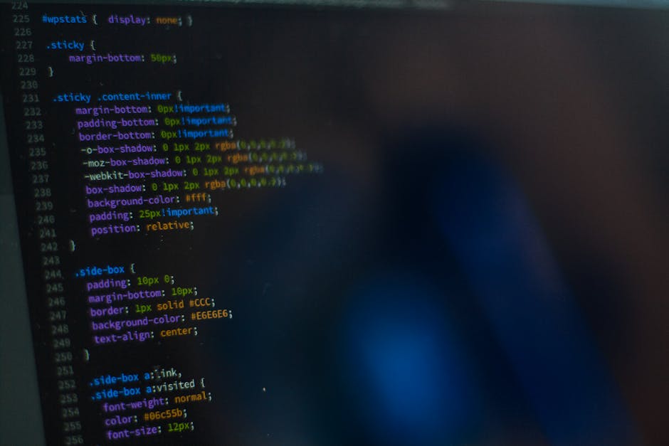 A close-up photograph of a computer screen displaying lines of colorful code in a text editor, with syntax highlighting in shades of blue, green, yellow, and purple. The code includes CSS properties a